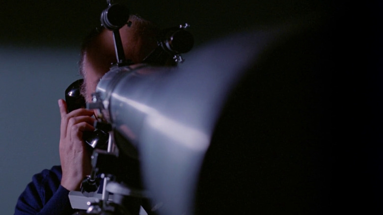 Leigh's stalker on the phone while watching through a telescope
