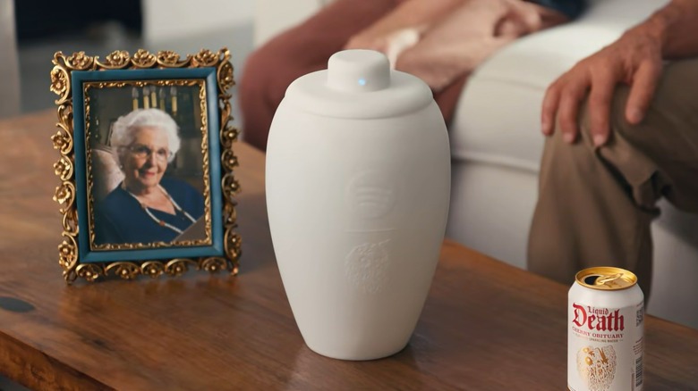 A family gathers around a coffee table, where a speaker urn sits between a grandmother's picture and a white Liquid Death Cherry Obituary can.