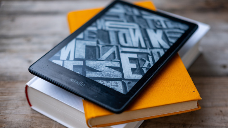A Kindle reader on top of a stack of books.