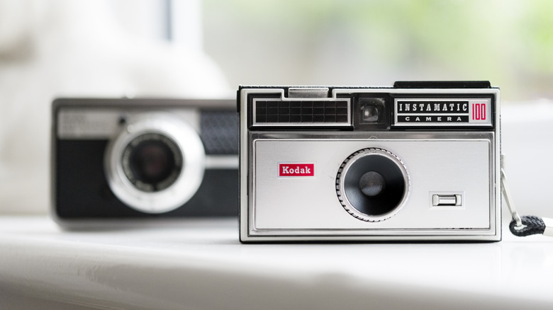 Close-up of two Kodak Instamatic point-and-shoot cameras on a well-lit shelf.