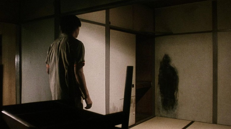 A scene from J-horror movie "Pulse" where a character is staring at a human-shaped black stain on the wall