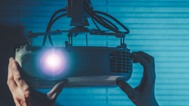 A person adjusting a home projector hanging from the ceiling.