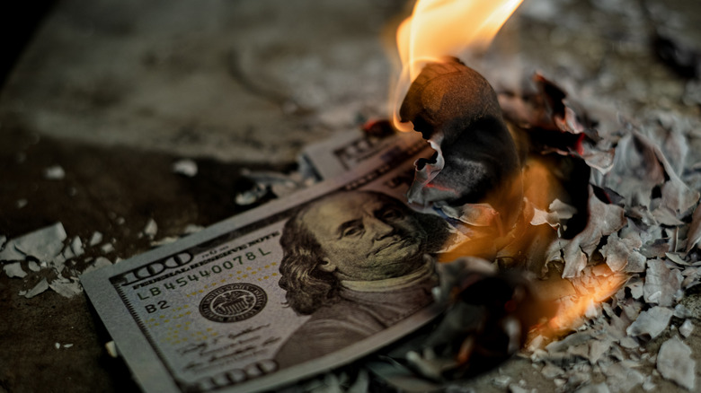 a one hundred dollar bill on fire symbolizing losing money