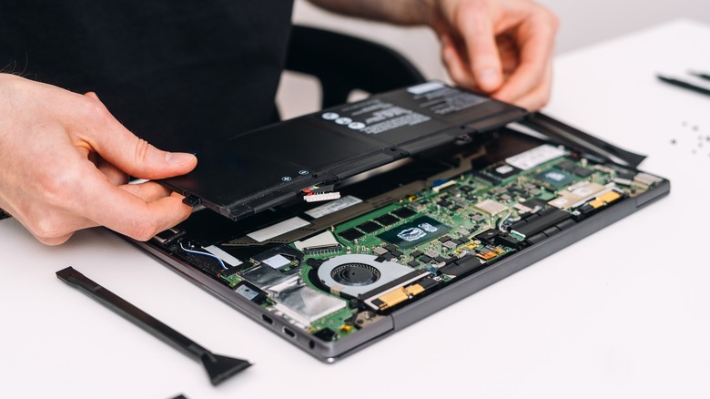 Repair technician holding a laptop battery over an open laptop