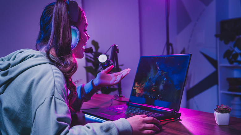 A woman playing DOTA 2 on a gamding laptop under purple lighting