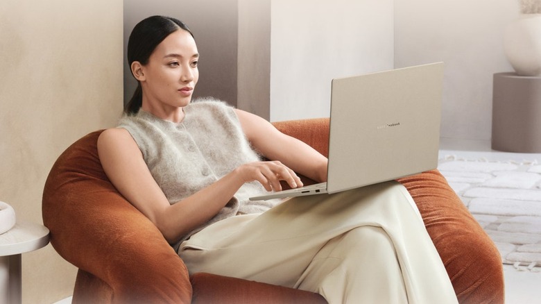 A woman sitting on a chair with an Asus Zenbook A16 notebook in her lap