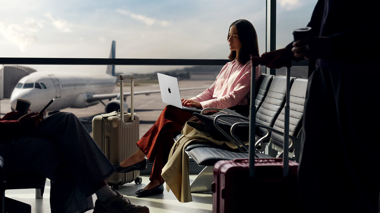 A woman sitting at the airport is working on an Apple MacBook Pro 14 M5 laptop.