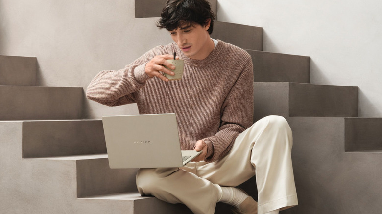 A man is sitting on a concrete staircase with an ASUS Zenbook A14 laptop on his knee.