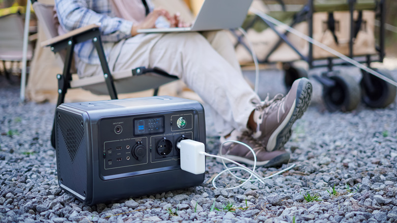 A person using a large power bank to power his laptop at a campsite