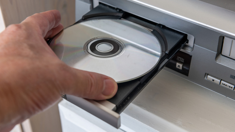 Someone inserting a DVD into a DVD player via an open disc tray.