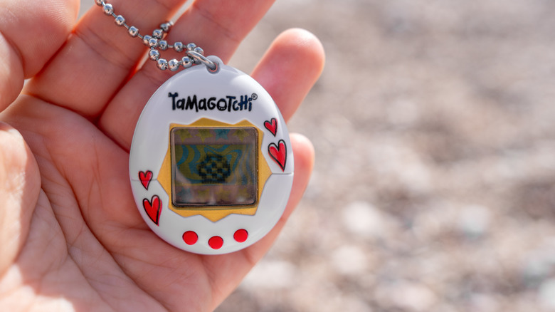 Close up of a Tamagotchi virtual pet keychain gadget in someone's hand.