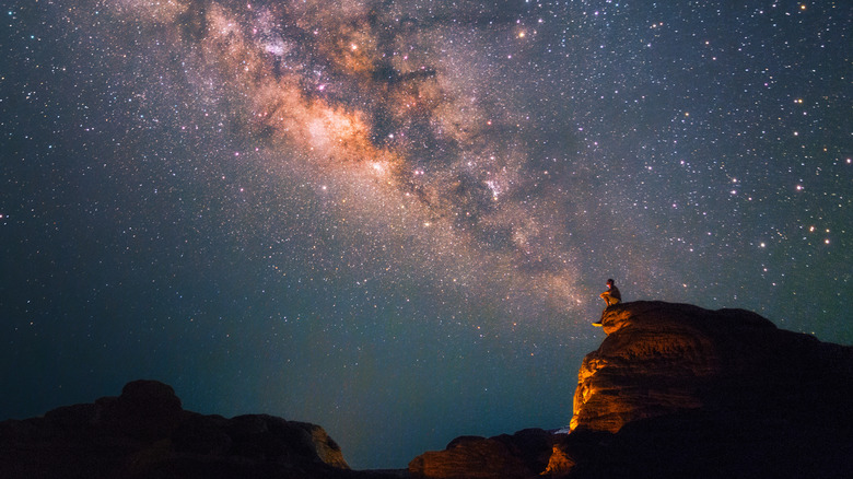 A person on a mountaintop looking at a starry sky and enjoying astronomy
