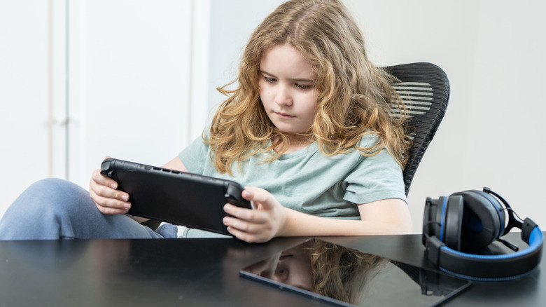 Child using a Nintendo switch with a tablet laid on the desk beside them
