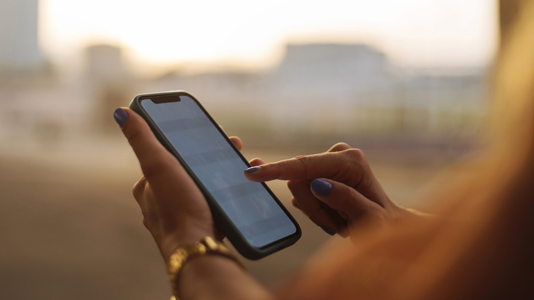 Someone using their phone outdoors with the bright sun in the background.