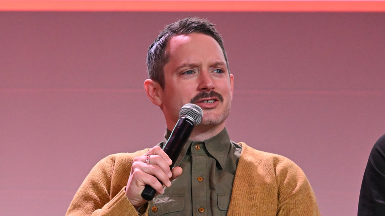 Elijah Wood with microphone on stage at fan event.