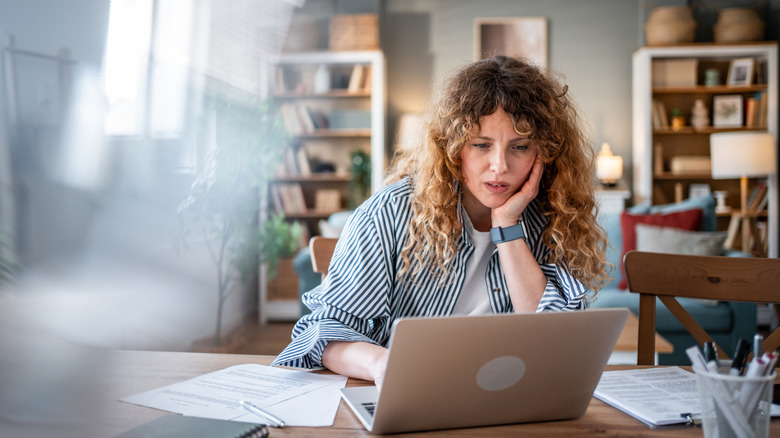Woman with curly hair using a laptop at a wooden table
