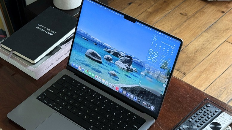 A MacBook pro on a table with some notebooks and TV remotes around it.