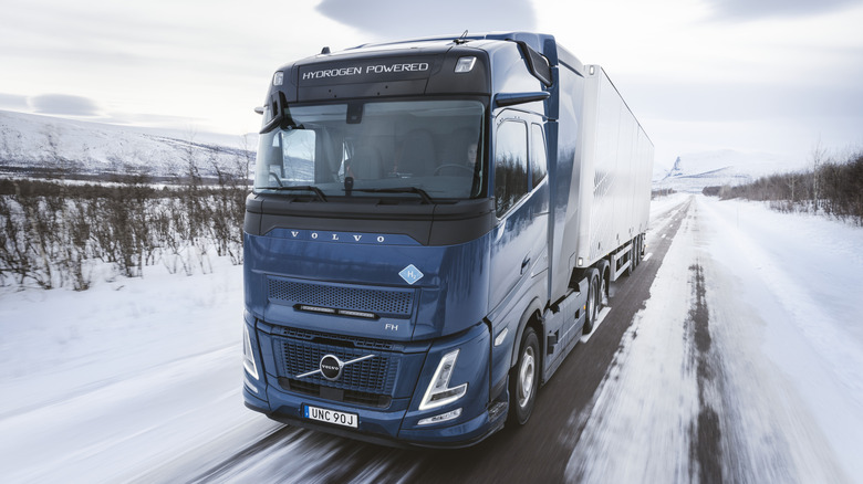 A blue hydrogen powered Volvo truck drives through a snowy landscape.