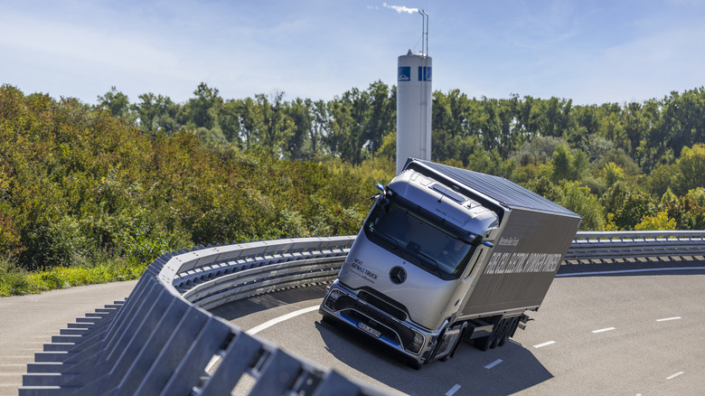 Mercedes-Benz's NexGenH2 Daimler hydrogen truck takes a bend along a wood lined road.