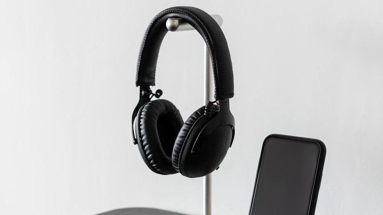 A headphone hanging on a silver stand kept next to a smartphone