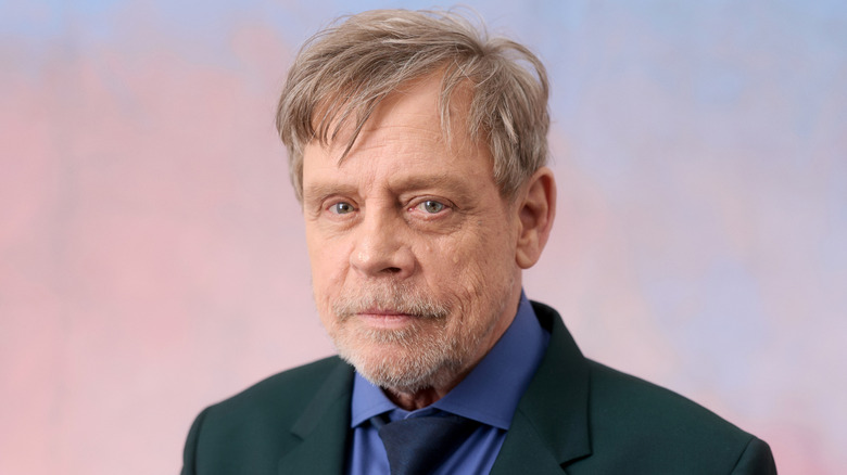 A close up of Mark Hamill against a pinkish blue background