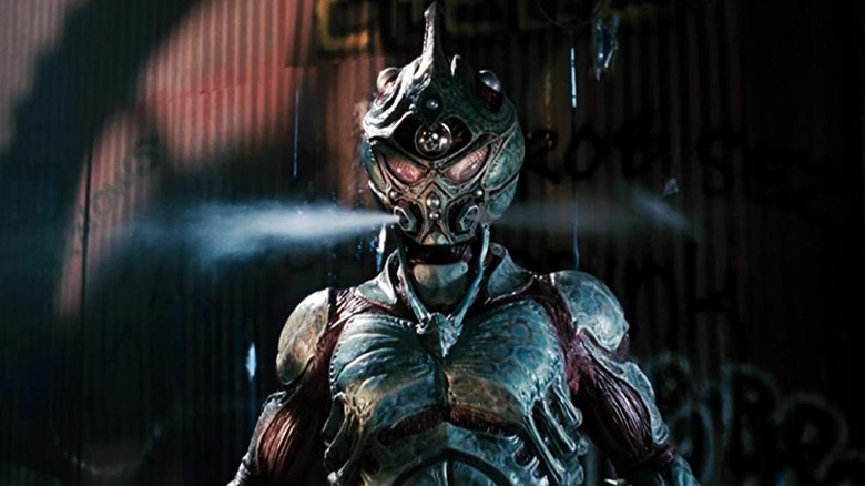 The Guyver standing in front of a graffiti wall with steam coming out of his mask.