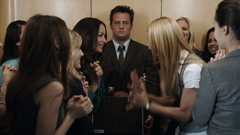 Mike standing grumpily in an elevator surrounded by women