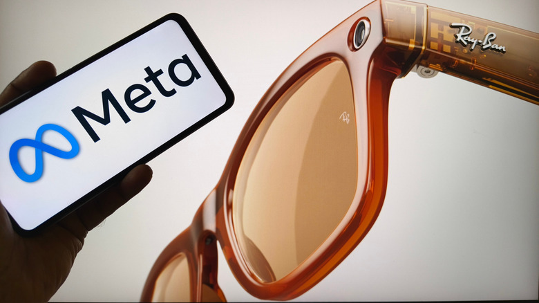 A smartphone displaying the Meta logo in front of a promotional image of Meta Ray-Ban glasses