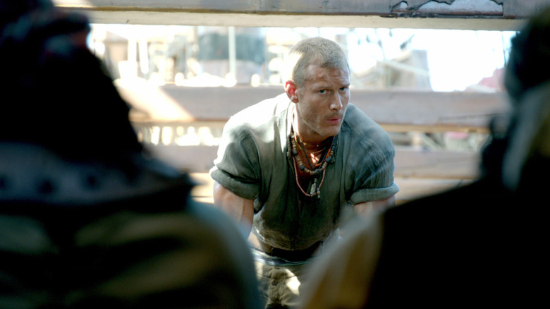 A character from the Black Sails series sitting on a bench with people in the foreground