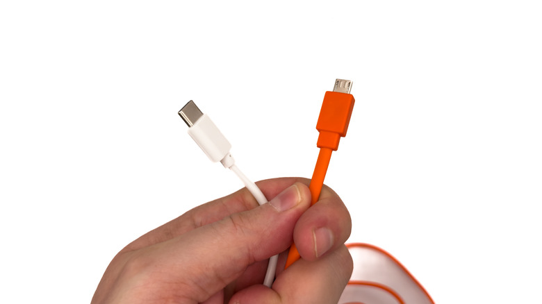 A hand holding a white USB-C cable and an orange Micro-USB cable side-by-side.