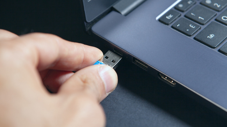 A hand plugs in a small USB flash drive into a laptop.