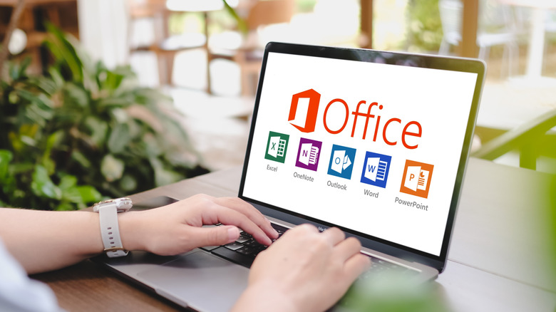 A woman sitting in a cafe using a computer with Microsoft Office logos on the screen
