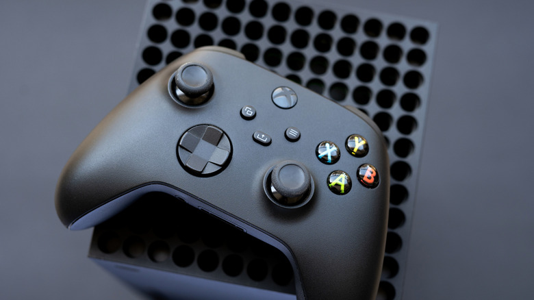 A black Xbox controller sitting on what appears to be the top of a Microsoft Xbox system, both items sit against a dark grey backdrop