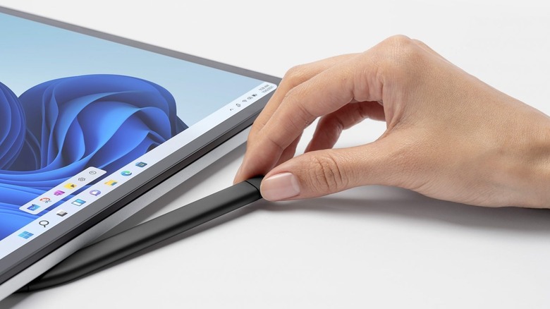 Close-up of a person holding a stylus next to Surface Laptop Studio on a gray background