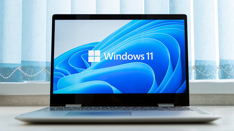Windows 11 logo on a laptop in front of a window