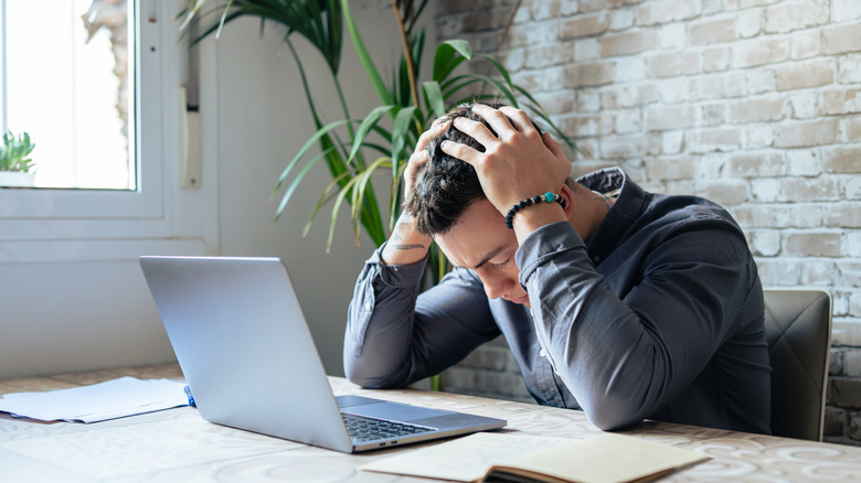 A man holding his head in his hands in front of a laptop computer