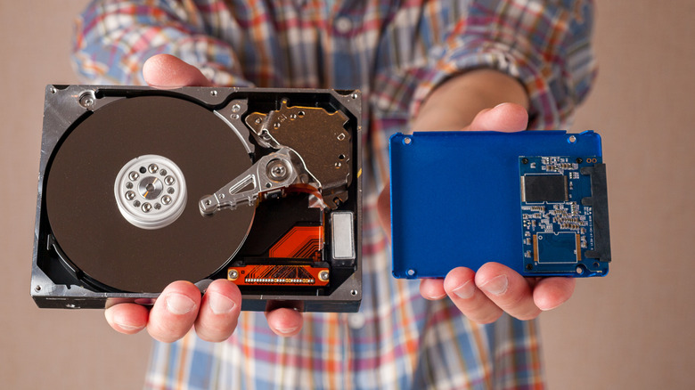 A man holding up an HDD in one hand and an SSD in another.