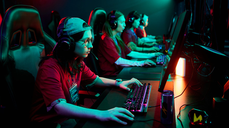 Esports players wearing headsets compete at gaming PCs under colorful neon lighting.