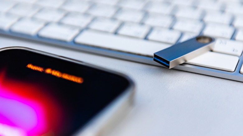 USB flash drive on a white keyboard with a phone nearby.