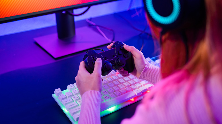Person using a game controller at a desk with RGB keyboard and monitor.