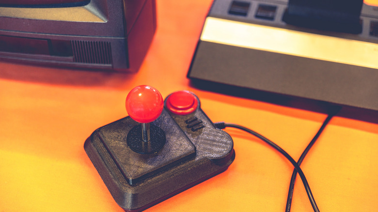 A retro gaming joystick with console and TV in the background