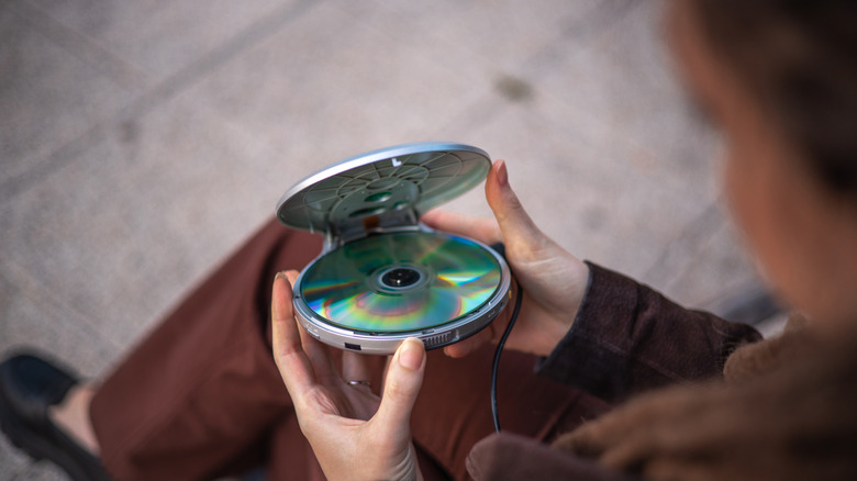 Person holding an open portable CD player with a disc inside, viewed from above.