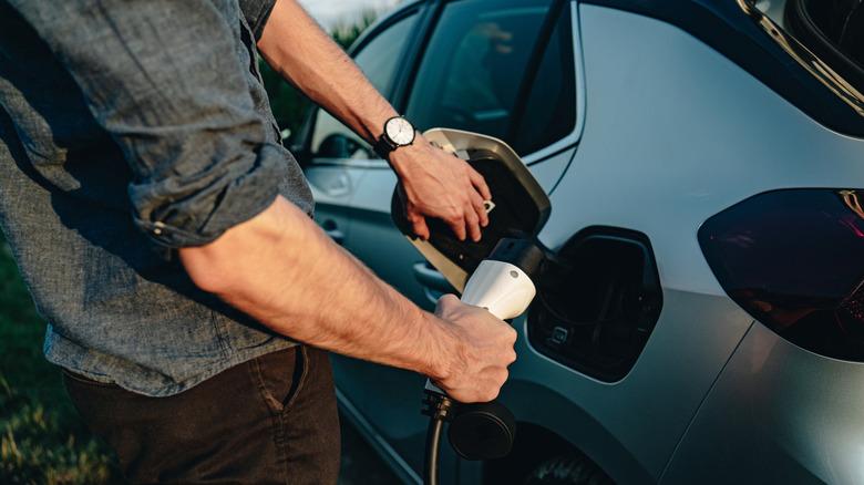 Close-up of a person plugging an electric vehicle charging cable into a car's charging port.