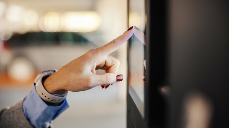 Close-up of a person's hand with painted nails tapping on a touch screen display.