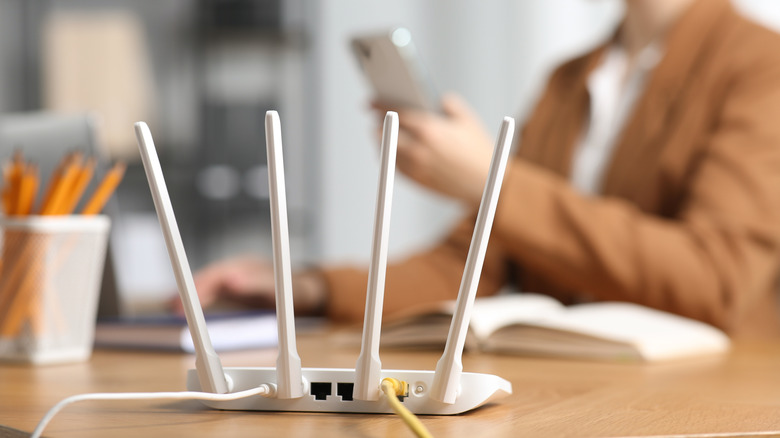 Wireless router on desk in foreground with someone on their phone in the background.