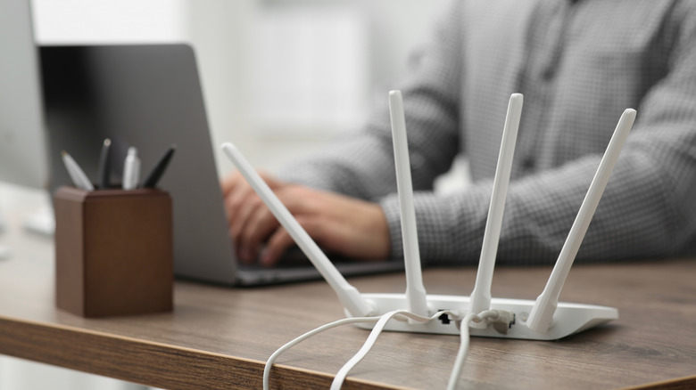 Someone working on laptop in background with wireless router in foreground.