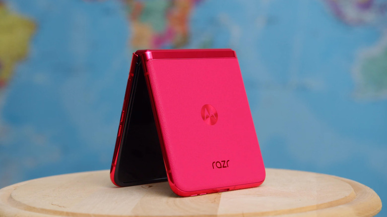 A pink Motorola Razr Fold smartphone sits folded in half with a map of the world behind it