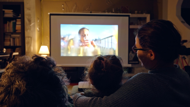 A family watches a movie at home using a projector.