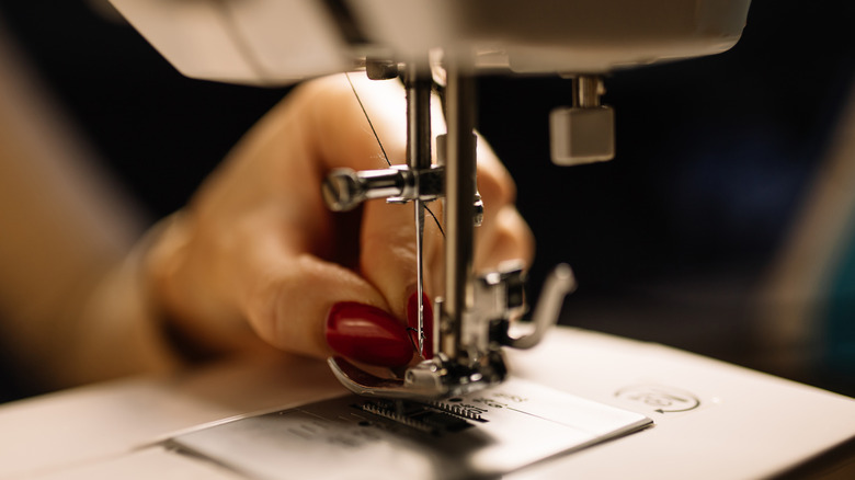A hand with bright red nail polish working with a sewing machine