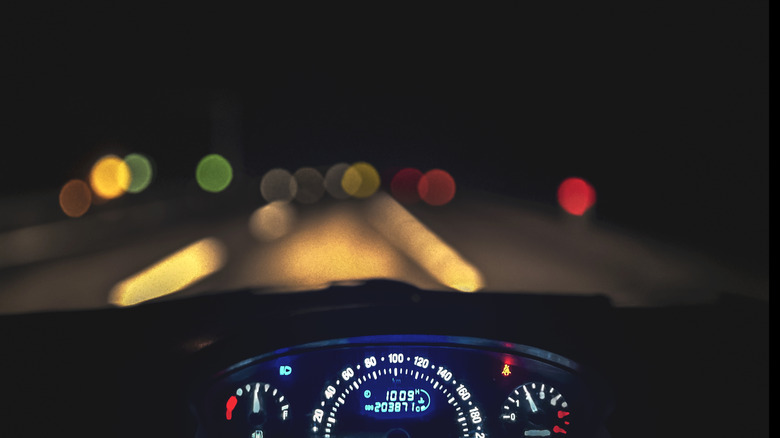 A car dashboard and speedometer light up against a dark night.
